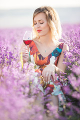 Beautiful blonde sexy woman is drinking red dry wine in lavender field