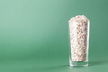 Raw oatmeal in a glass on a green background