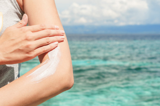 Young Caucasian Woman Applying Sun Protector Cream At Her Hand On The Beach Close To Tropical Turquoise Sea Under Blue Sky