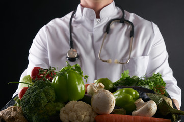 Doctor nutritionist holding tray with heart healthy foods vegetables and fruits on black...