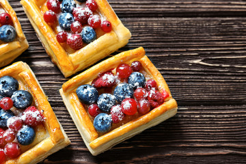 Delicious puff pastry dessert with berries and sugar powder on wooden background