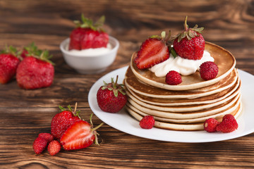 Delicious pancakes with strawberries and cream and in cream on a brown wooden background