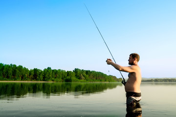 fisherman fishing in a calm river in the morning. Man in fishing gear stending in a river and throws a fishing pole