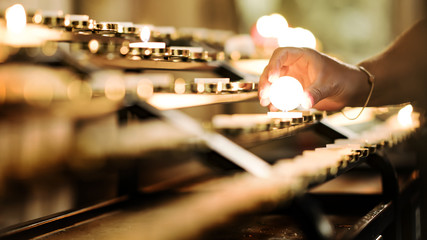  A woman lights a candle in a church. Beautifully blurred background.