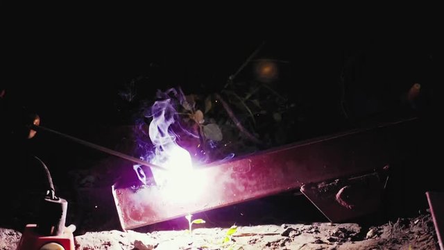 Flashes and lot of sparks from welding work at construction site in dark in slow motion