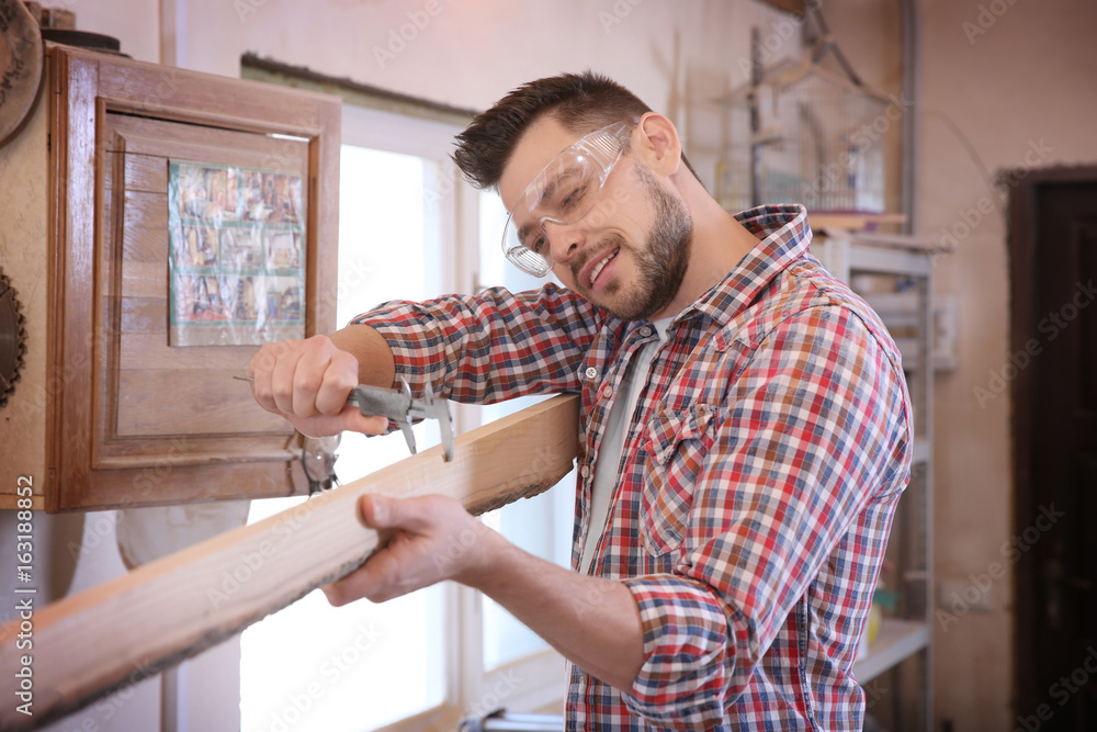 Wall mural carpenter measuring wooden plank in workshop