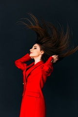 Young gorgeous model in red coat throwing her hair on dark background