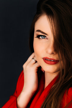 Expressful portrait closeup of young woman in red clothes with red lips on dark background