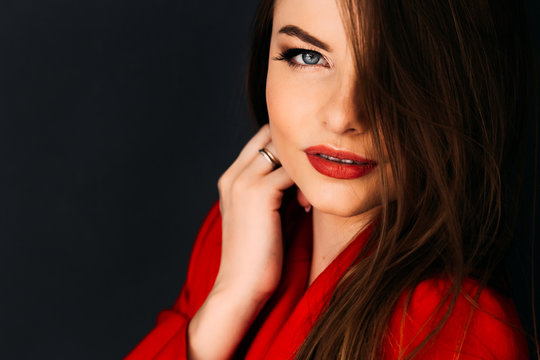 Beautiful model  in red jacket with red lips on dark background holding her hand on her hair