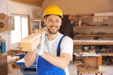 Smiling carpenter carrying timber in workshop