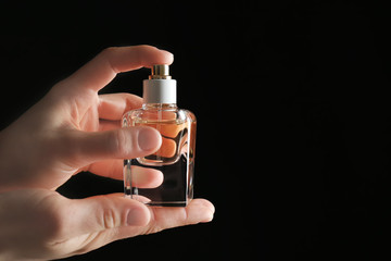 Female hands holding bottle of perfume on black background