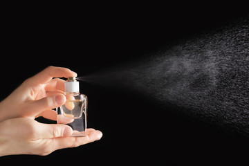 Female hands spraying perfume against black background
