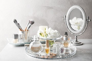 Composition of glass tray with perfume bottles and cosmetics on grey table
