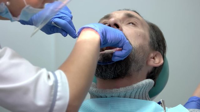 Patient with dental mouth opener. Work of dentist in gloves.