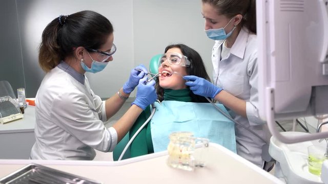 Two stomatologists busy with patient. Lady in dental safety glasses.