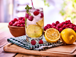 Cold non alcoholic cocktails with lemon slice and raspberries with mint leaf. Lemonade ice cubes. Nonalcoholic beverage on wooden board. Table setting rural style with cooling summer drink homemade.
