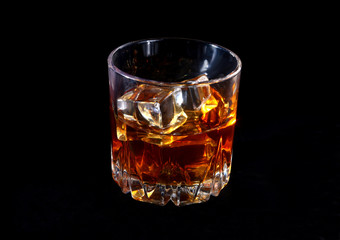 Glass of whiskey or bourbon with ice on black stone table.