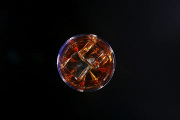 Glass of whiskey or bourbon with ice on black stone table. Top view.