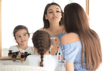 Young woman and her little daughter applying makeup at home