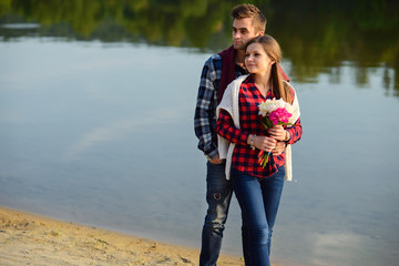 Stylish young smiling couple in shirts and jeans while walking on the shore of a lake.