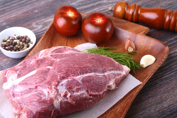 Raw pork steaks on wooden board with herbs, spices, tomatoes and pepper grinder ready for cooking. Selective focus