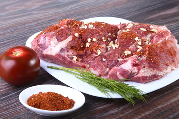 Raw pork steaks on wooden board with herbs, garlic, spices and tomatoes ready for cooking. Selective focus.