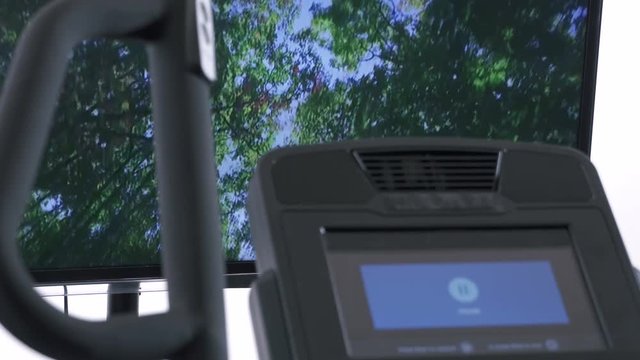 Elliptical cardio workout in front of the television. TV screen displaying interactive trail through the forest.