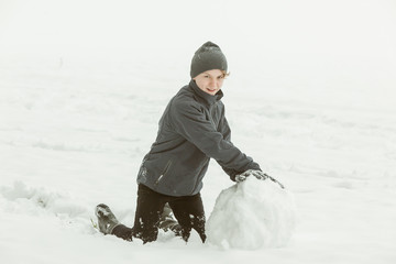 Fototapeta na wymiar Boy forming a large snowball outside