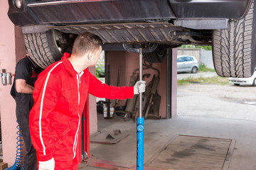 Young auto mechanic in uniform holding equipment for elevating car on a lift