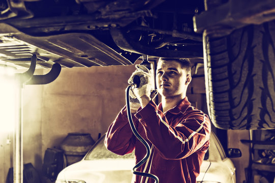 Professional handsome male auto mechanic in uniform working underneath a lifted car