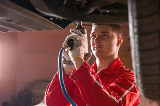 Professional handsome male car mechanic in uniform working underneath a lifted car