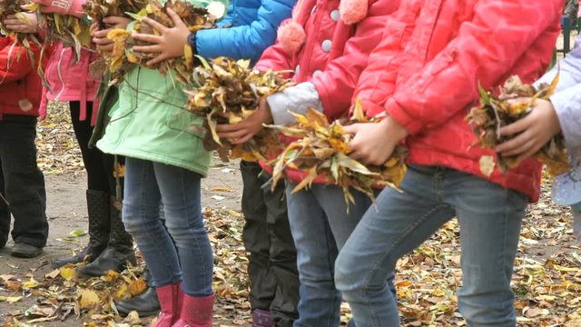 Large group of children throw yellow autumn foliage up outdoors