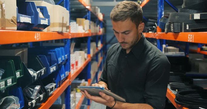 Delivery logistics manager working using tablet pc in a large orange-blue warehouse
