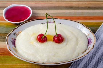 Milk porridge on a wooden multicolored background with cherries and jam.