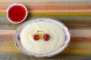 Milk porridge on a wooden multicolored background with cherries and jam.