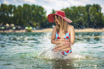 Attractive blonde woman playing in the clear sea water on the beach, enjoying summertime