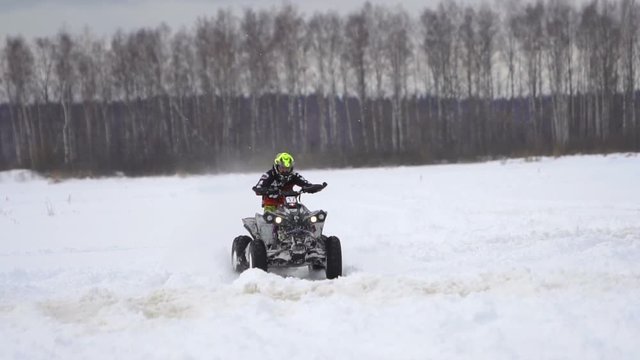 ATV race on the snow. Rider driving in the quadbike race. Man riding ATV in sand in protective clothing and a helmet. Racer rides a quad motorbike in the cross racing. Quadrocycle on the snow cover