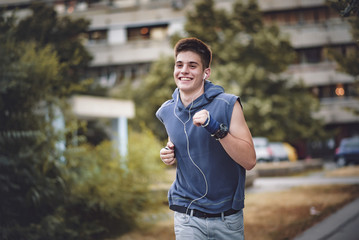 Young healthy man jogging outdoor in a park and listening to music