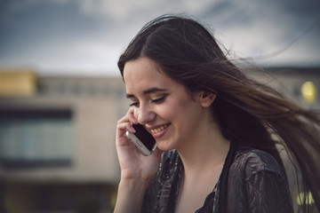 Happy young woman having a cheerful conversation over her phone on a windy weather