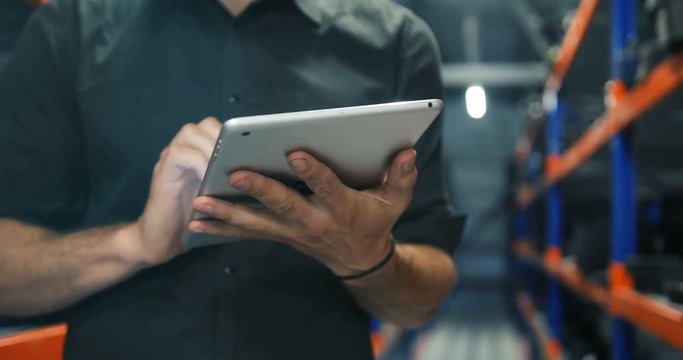 closeup businessman In strict dark-grey shirt hands using tablet pc in warehouse perspective
