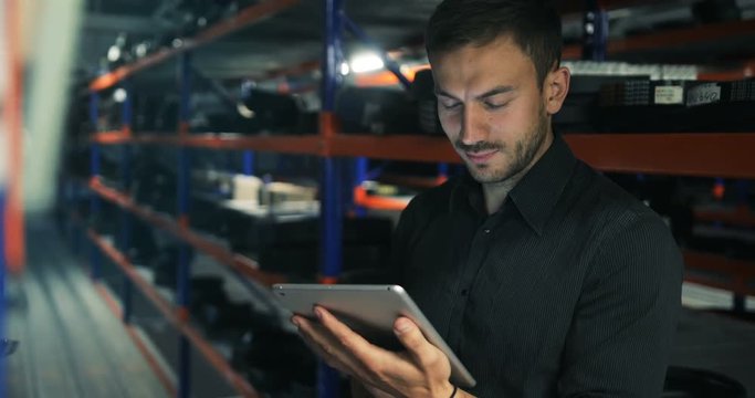 Standing worker smiling at camera while holding digital tablet in warehouse perspective