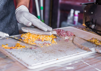 Chef at a street market preparing sandwich with grilled melted cheese and bacon