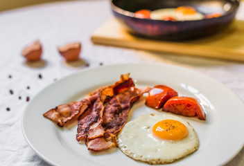 Fried chicken eggs with crispy bacon and tomatoes against white background