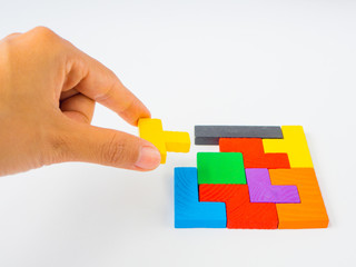 hand holding the last piece to complete a square tangram puzzle colorful wooden puzzle for kid on white background