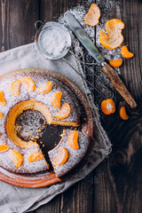 Homemade Citrus Tangerine cake decorated with icing sugar and slices of mandarin on wooden table background. Close up Christmas holiday cake