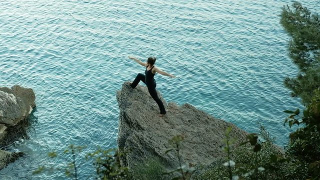 Woman standing in profile training chest, arms muscles yoga outdoors. Shooting top female with perfect body, actively carry out exercises stand on rock under water lake. Beautiful, charming, fit Lady