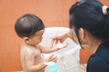 Obraz na płótnie Canvas Asian mother teach her baby to take a shower by himself
