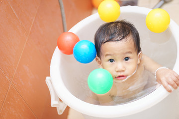 A year old and 5 months Asian baby play a ball while taking a shower