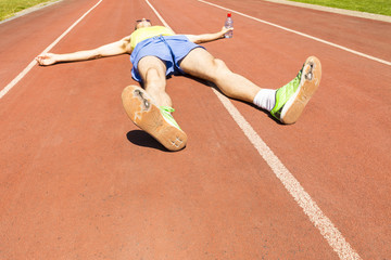 An exhausted athlete on a running track wearing broken green running shoes with big holes in the...