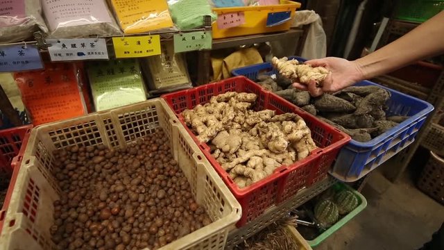 Baskets with curcuma zedoaria, herbs and cactus in an herbalist. A herbal shop in Herb Alley, located close to Lungshan Temple in Taipei, Taiwan. A person is touching them.